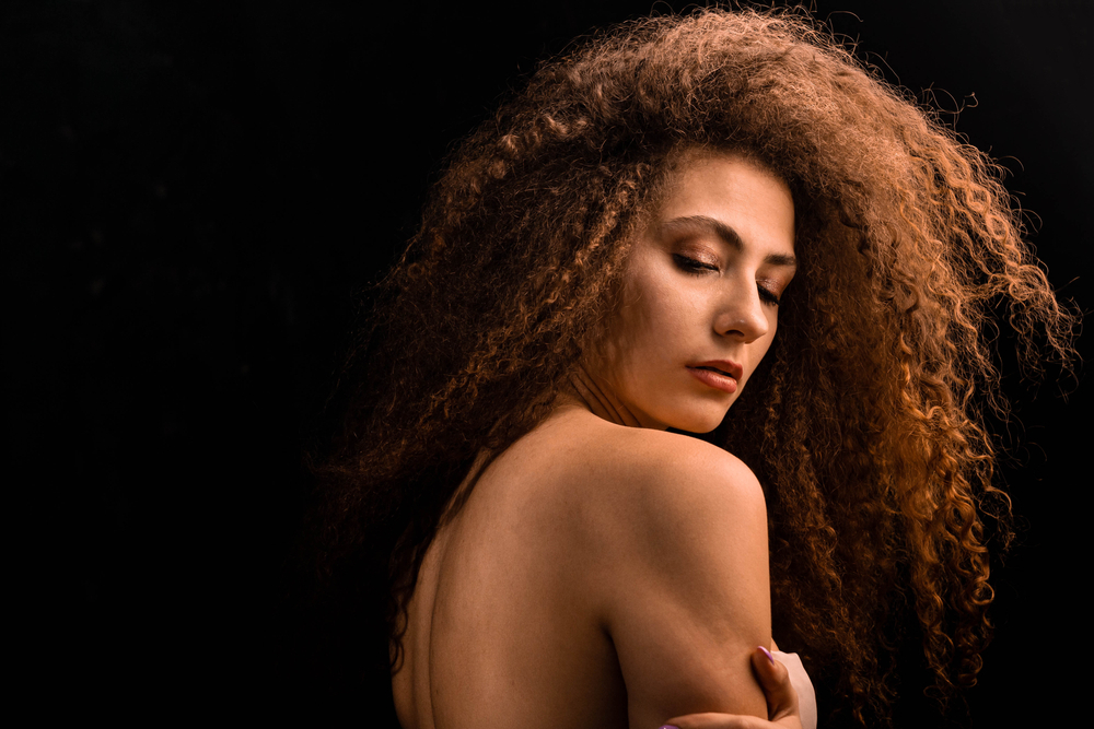 Woman with wavy brown natural hair looking over her shoulder
